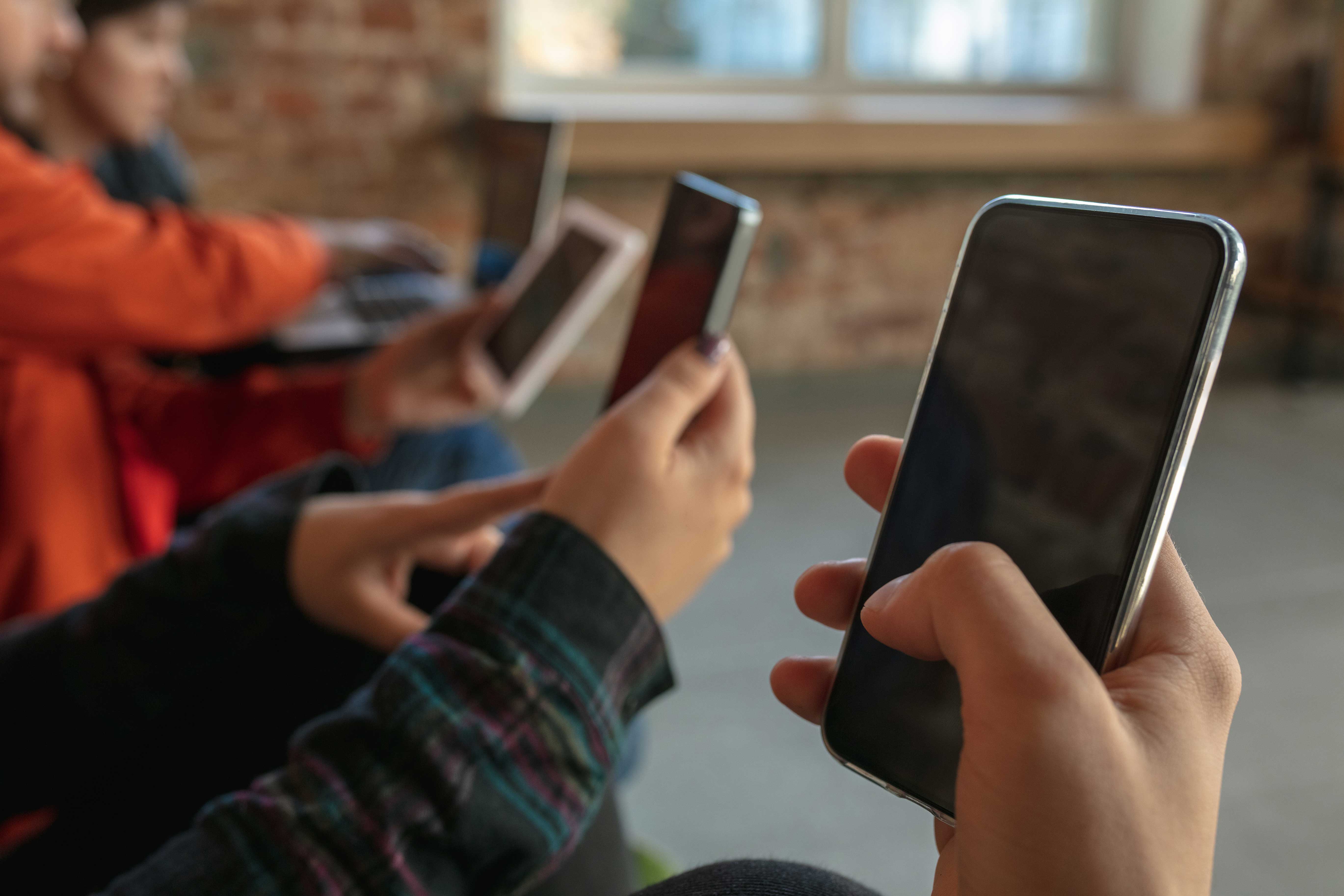 Tips Memilih Smartphone untuk Bermain Mobile Legends 10 group happy young young people sitting sofa together sharing news photos videos from smartphones reading articles playing games having fun social media modern technologies